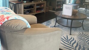 Un salon comprenant un canapé, un téléviseur, une table basse et une pancarte sur laquelle on peut lire : « Bienvenue à Cape Vista ».
