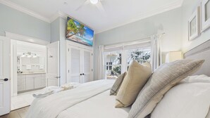 A bedroom with a bed, pillows, a painting, a bathroom with a vanity, and a view through a window. - Sundancer 101-Modern Retreat-Sleeps 6 (Santa Rosa Beach)