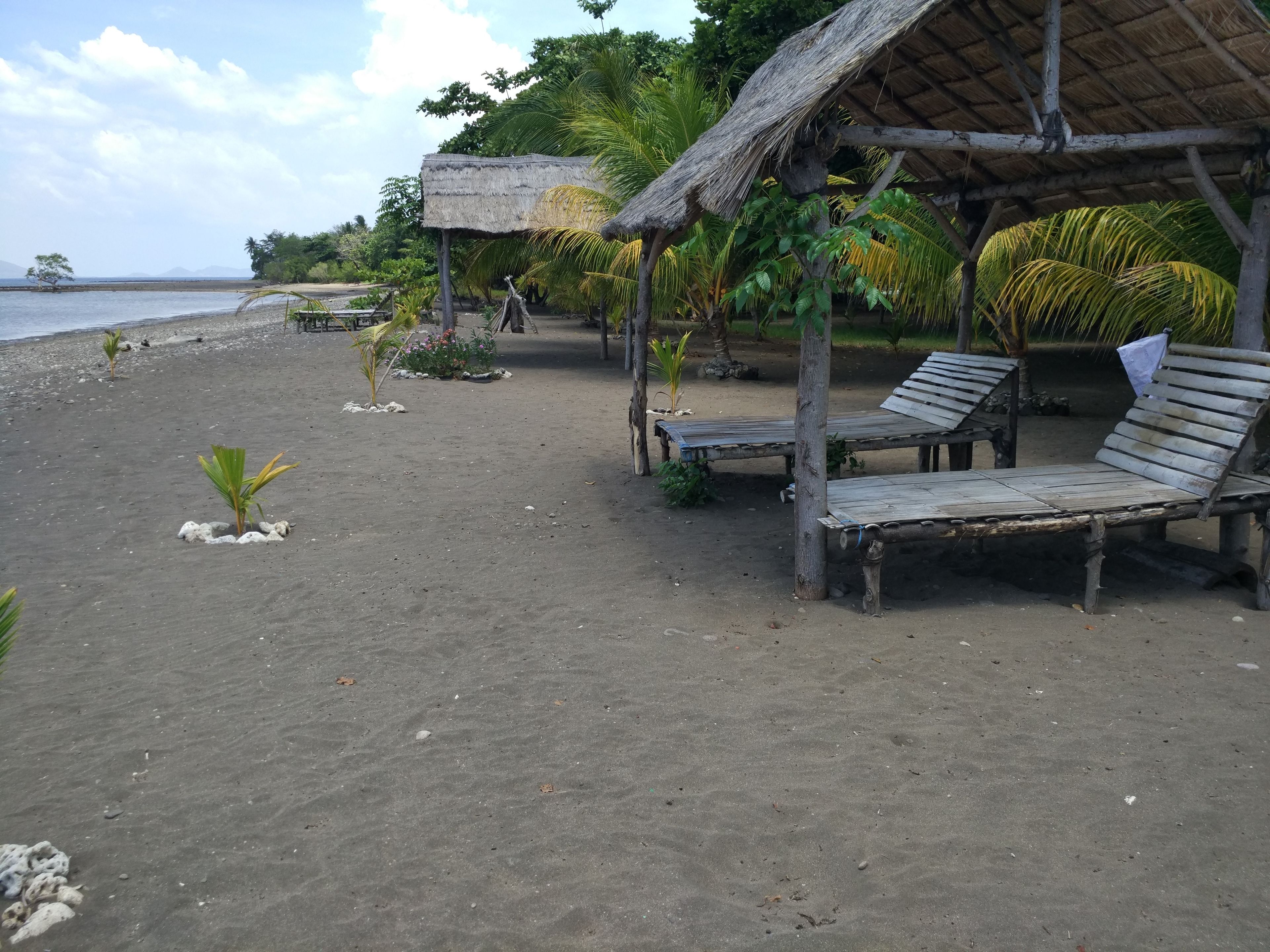 A beach with wooden lounge chairs and thatched-roof structures.