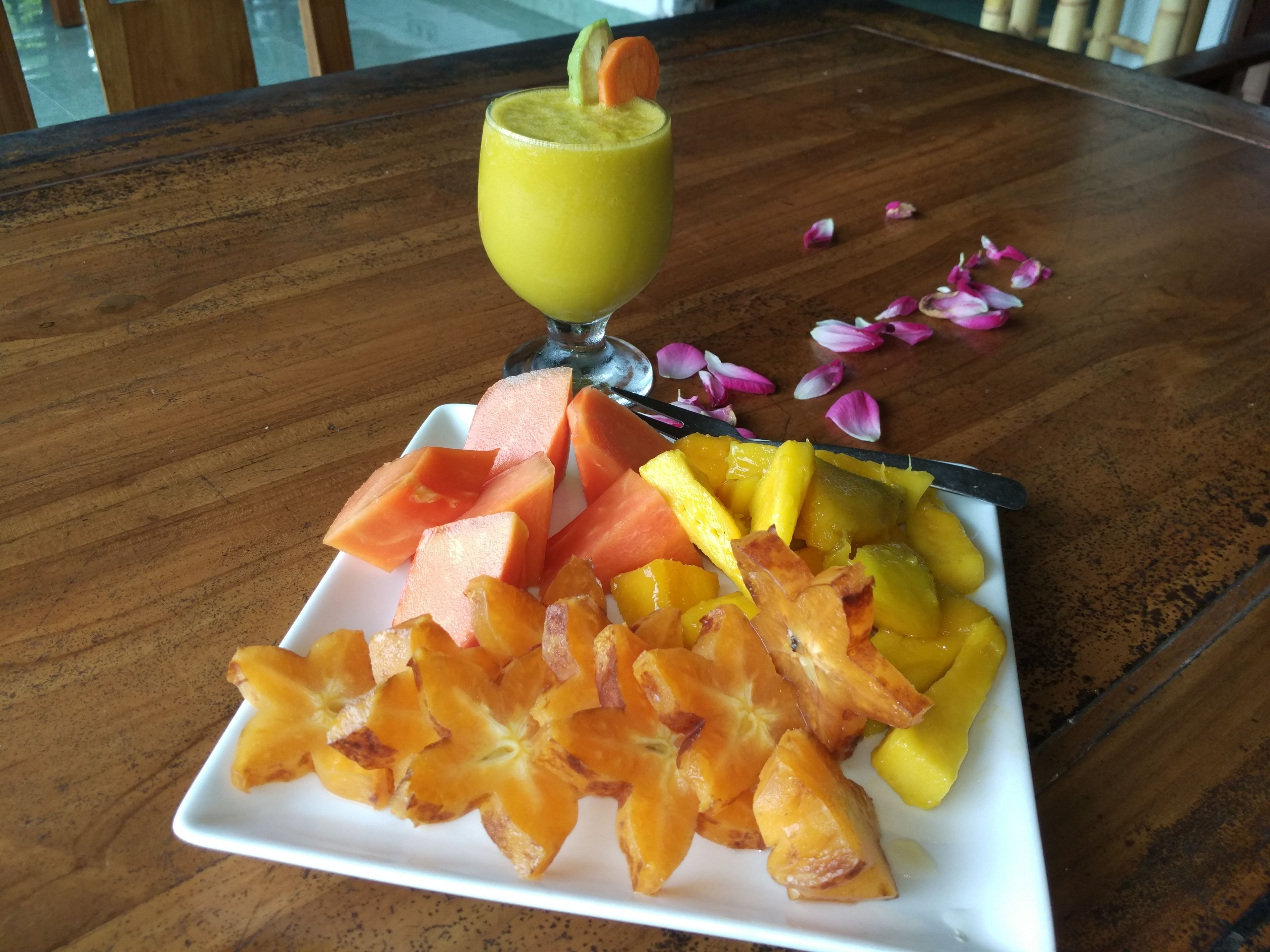 A plate of fruit and a glass of green juice on a wooden table.