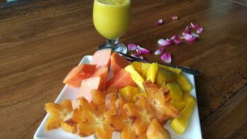 A plate of fruit and a glass of green juice on a wooden table.