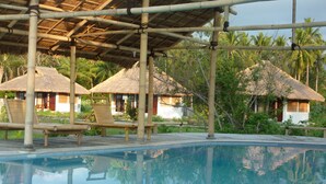 A pool area with bamboo structures and thatched-roof huts. - Budi Sun Resort (Maumere)