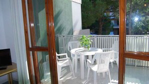 A balcony with a white table and chairs, a potted plant, and a view of trees and buildings. - Holiday apartment mit Klimaanlage und Pool (Lignano)