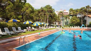 A swimming pool with lounge chairs and umbrellas, surrounded by trees and buildings. - Holiday apartment mit Klimaanlage und Pool (Lignano)