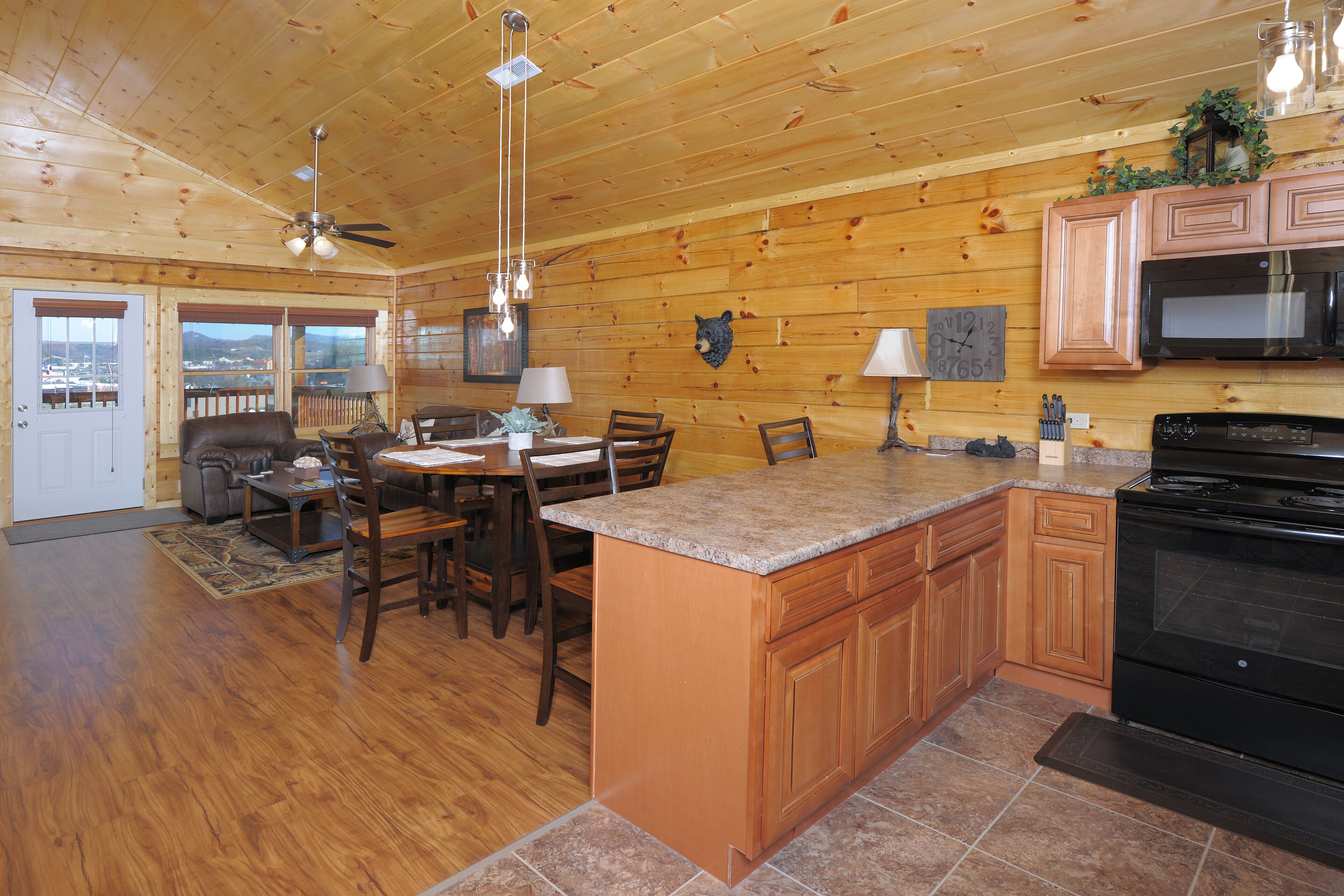 A spacious kitchen with wooden cabinets, a granite countertop, and a black stove. There is a dining area with a table and chairs, and a ceiling fan above.