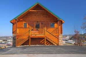 A log cabin with a green roof, a front porch with a railing, and a staircase leading to the entrance. - City Lights With A Heated Private Indoor Pool & The Very Best Views! (Pigeon Forge)