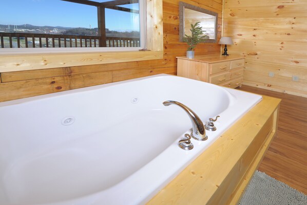 A wooden cabin with a large white bathtub, wooden walls, a window with a view, and a small plant on a wooden dresser. - City Lights With A Heated Private Indoor Pool & The Very Best Views! (Pigeon Forge)