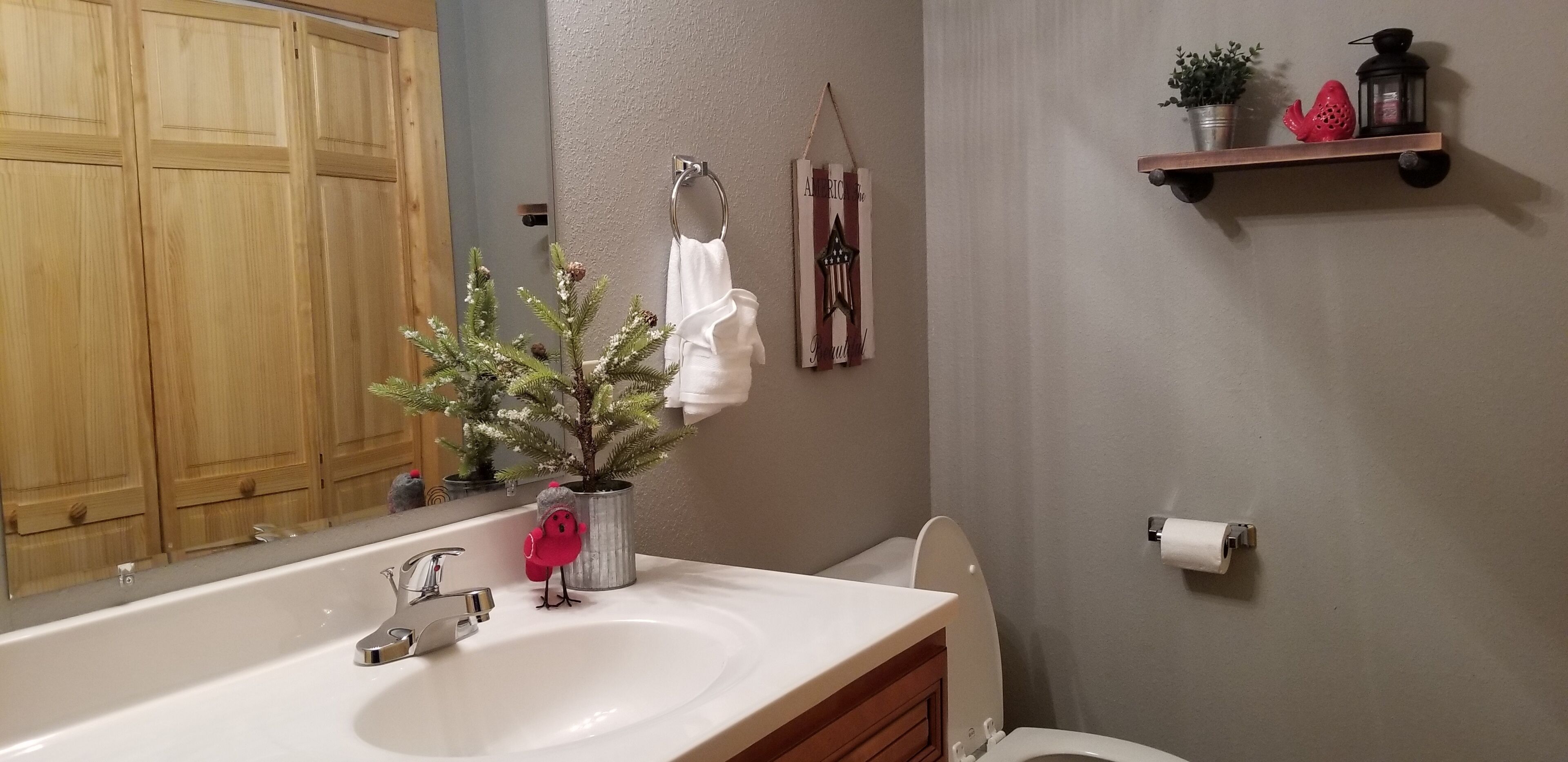 A bathroom with a wooden cabinet, a white sink, a potted plant, a hanging towel, and a shelf with decorative items.