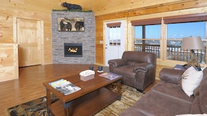 Una sala de estar acogedora con chimenea, mobiliario de cuero y ventanas amplias que ofrecen una vista.