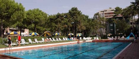 Una piscina con agua cristalina, rodeada de sillones de baño y sombrillas.