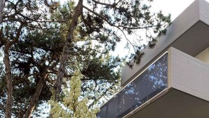 Un edificio moderno de dos pisos con balcones, rodeado de árboles y una planta grande.