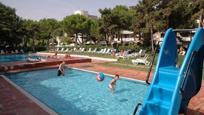 Una piscina con tobogán azul, sillas de descanso y sombrillas.