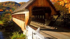 A wooden covered bridge with a white fence in front, surrounded by autumn foliage and hills. - Killington Mountain View Townhouse (Killington)