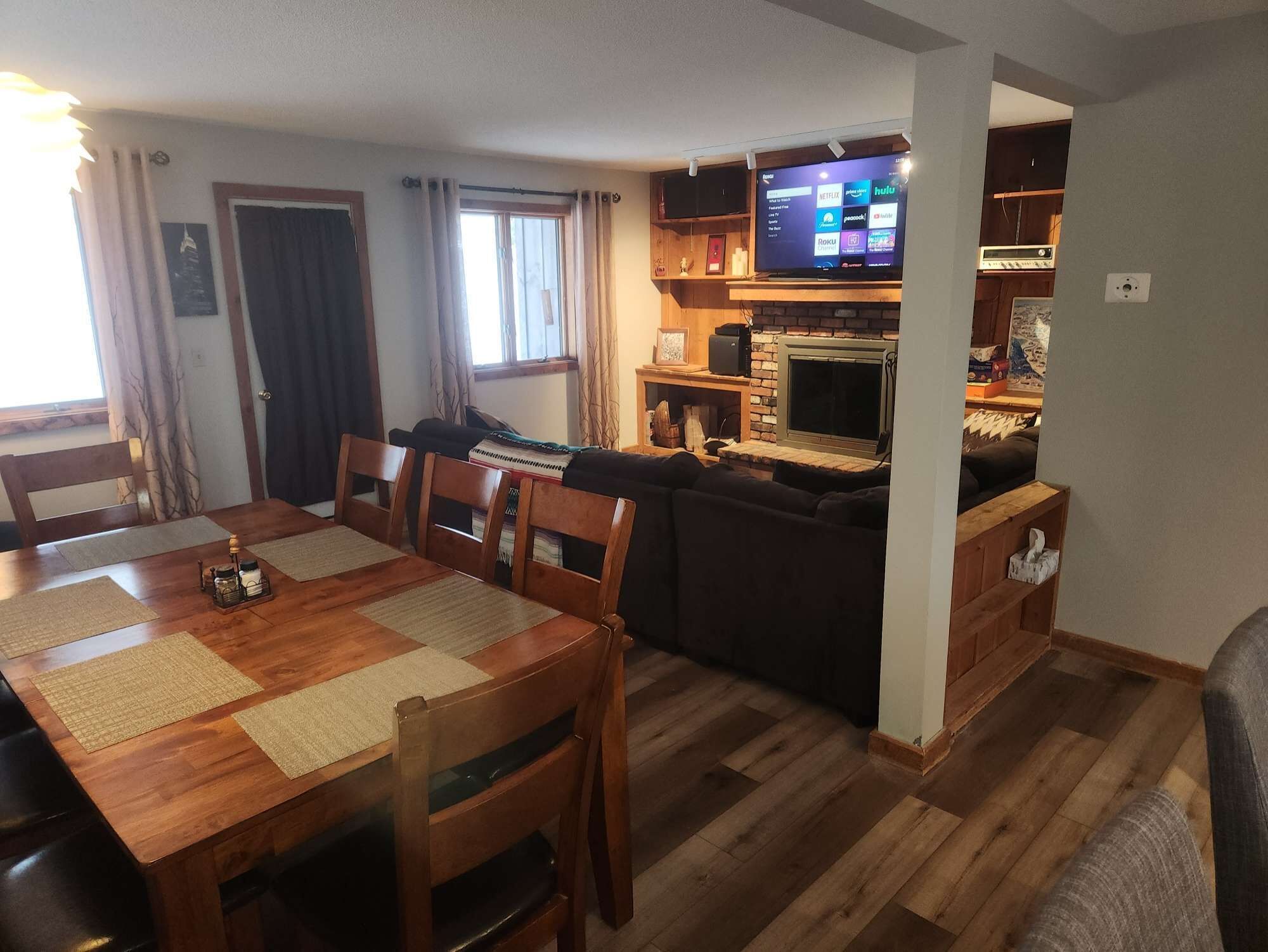 Ein gemütliches Wohnzimmer mit einem Holzesstisch, Stühlen, einer Couch und einem Kamin.