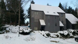 A two-story building with a sloped roof, surrounded by snow-covered ground and trees. - Killington Mountain View Townhouse (Killington)
