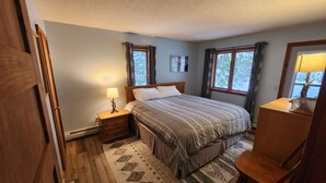 A bedroom with a bed, nightstand, chair, and a window with curtains. - Killington Mountain View Townhouse (Killington)