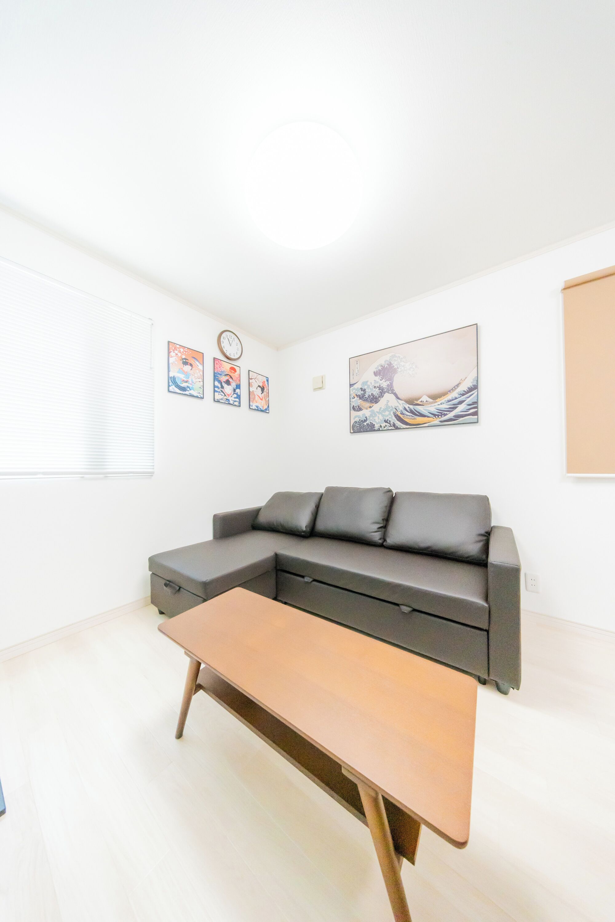 A modern living room with a grey sectional sofa, a wooden coffee table, and wall art including a clock and Japanese prints.