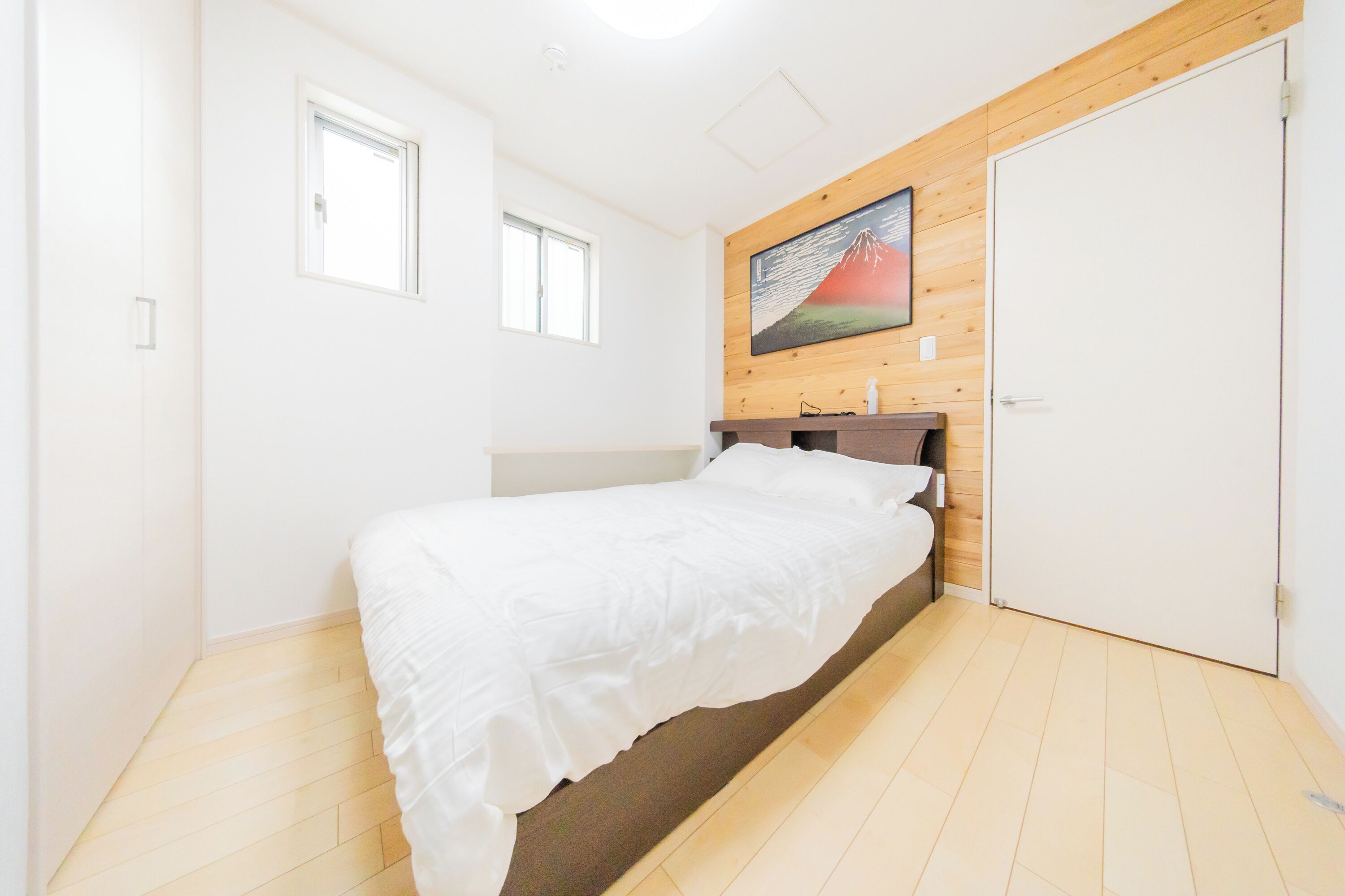Ein Schlafzimmer mit einem Bett, einem hölzernen Kopfende, einer weißen Tür und einem Fenster.