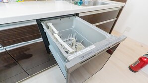 Eine Küche mit Geschirrspüler-Auszug, Holzschränken und einer roten Kanne auf der Arbeitsplatte.