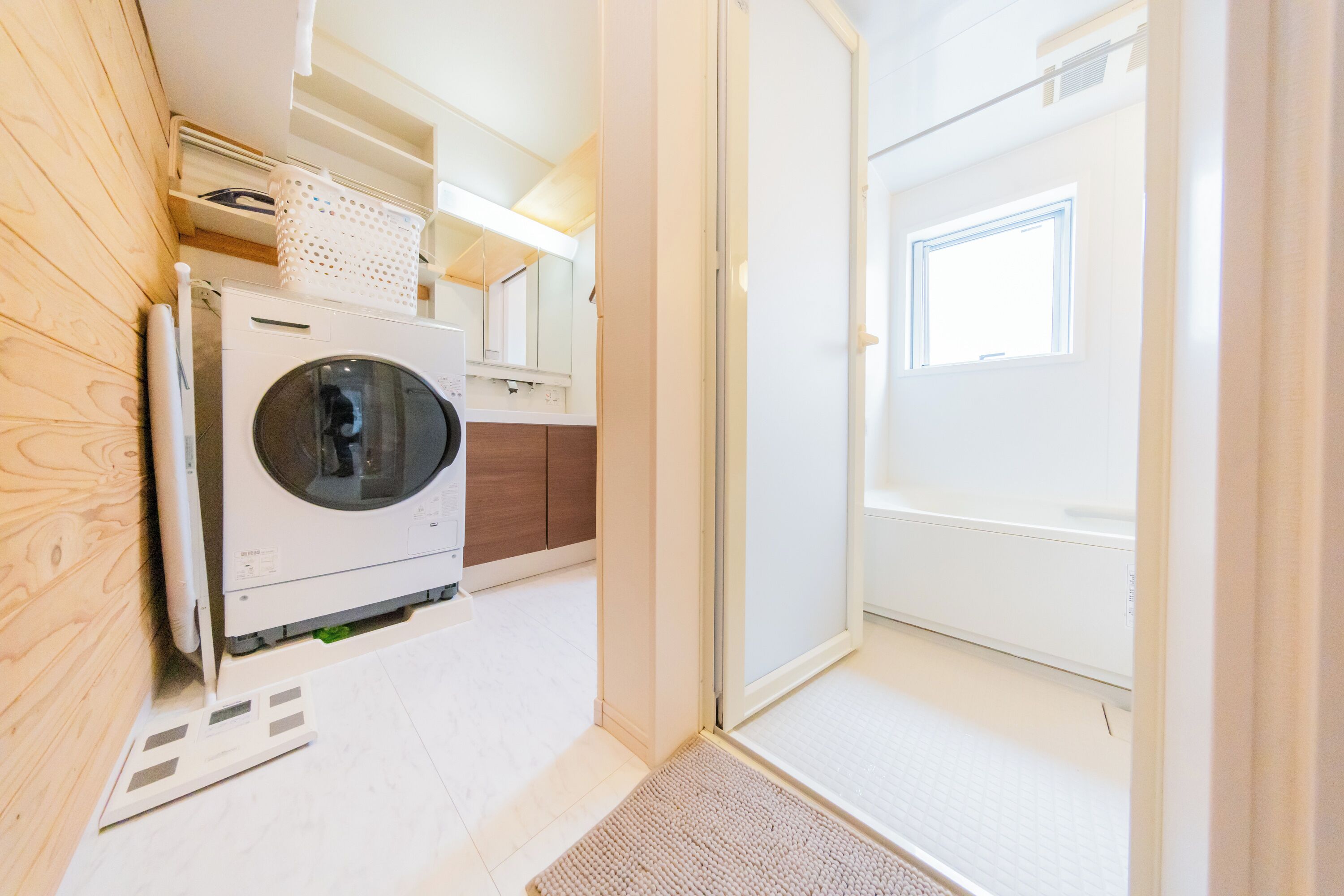 A laundry room with a front-loading washing machine, wooden cabinets, and a door leading to another room.