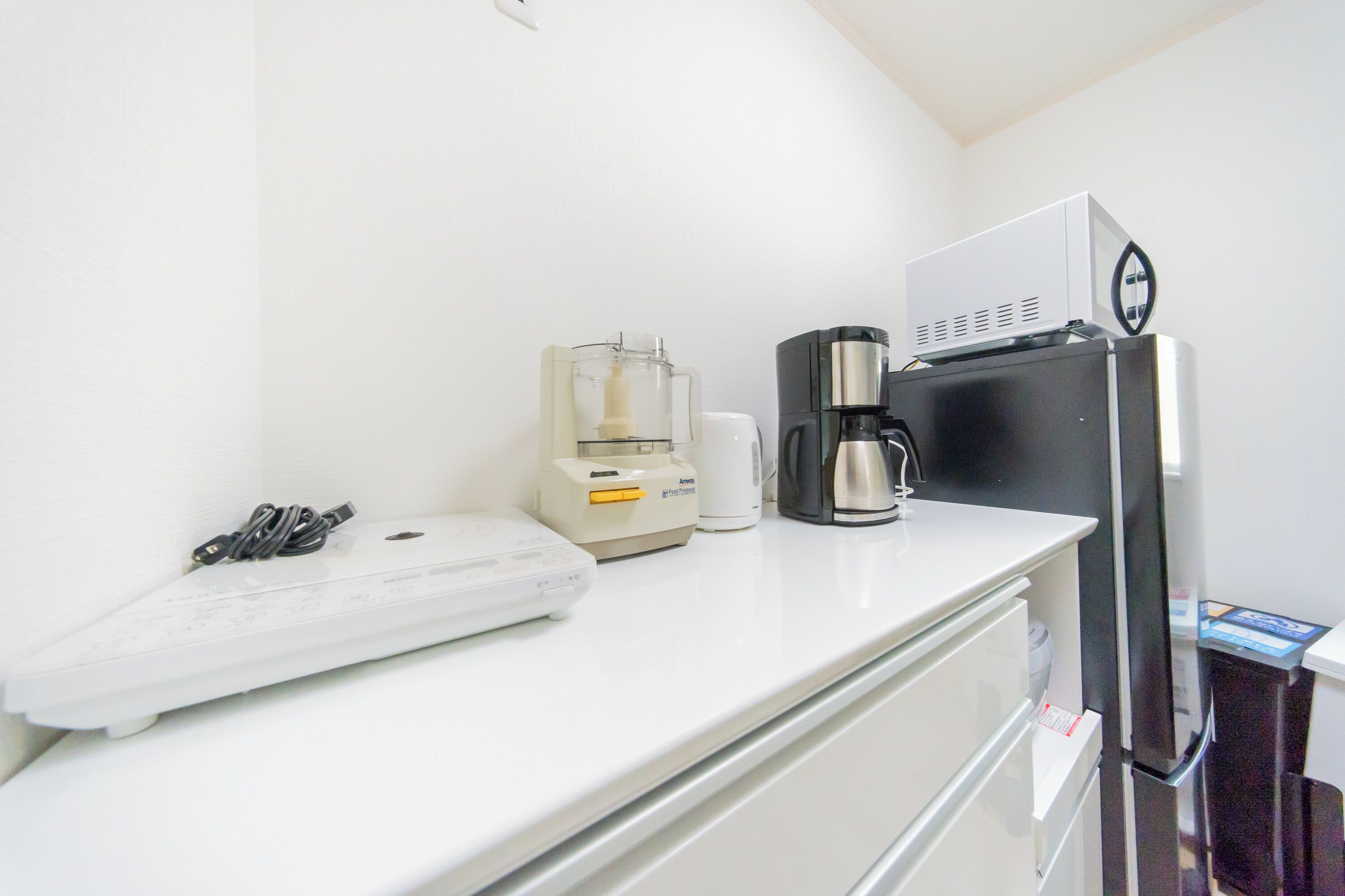 Una kitchenette con cafetera, electrodoméstico pequeño y microondas sobre la encimera.