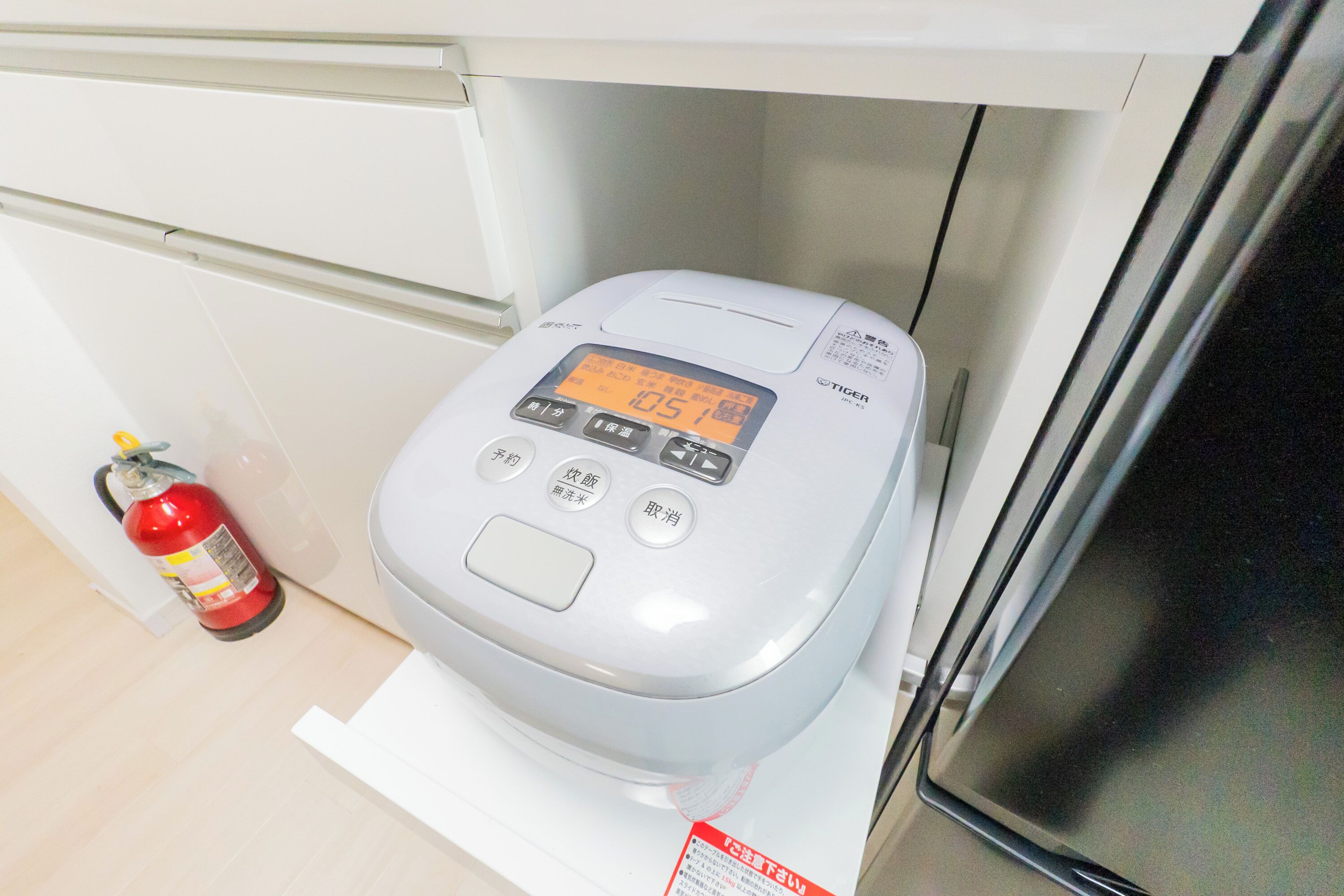 En modern toalett med en digital display och en kontrollpanel, placerad i ett rent och minimalistiskt badrum med en vit handfat och en synlig brandsläckare.