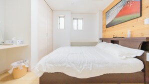 Ein Schlafzimmer mit Bett, Holz-Kopfteil, einem Bild an der Wand und einem Fenster.