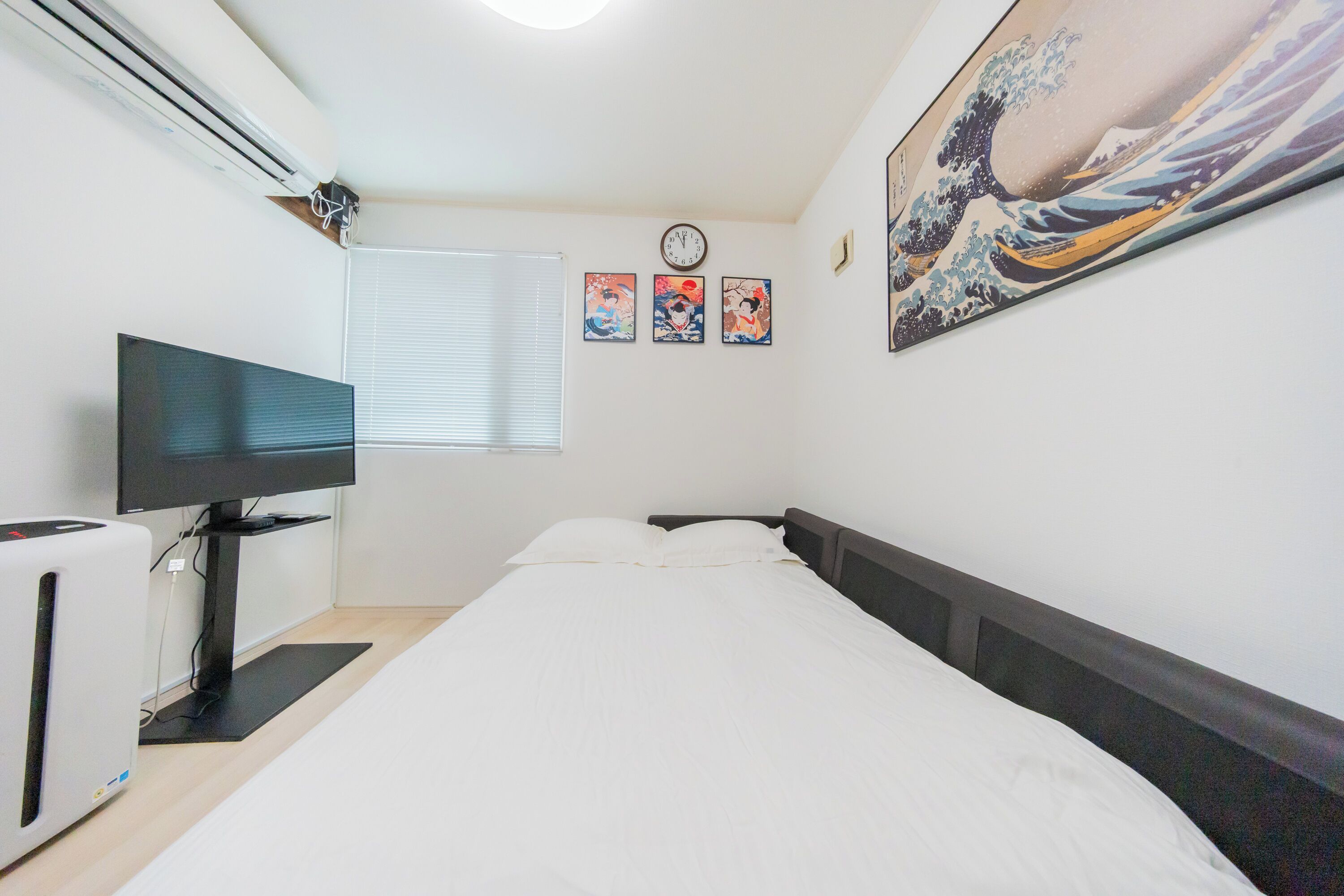 A bedroom with a bed, a TV, an air conditioner, and wall art.