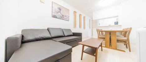 A modern living room with a grey sectional sofa, a wooden dining table with chairs, and a minimalist decor.