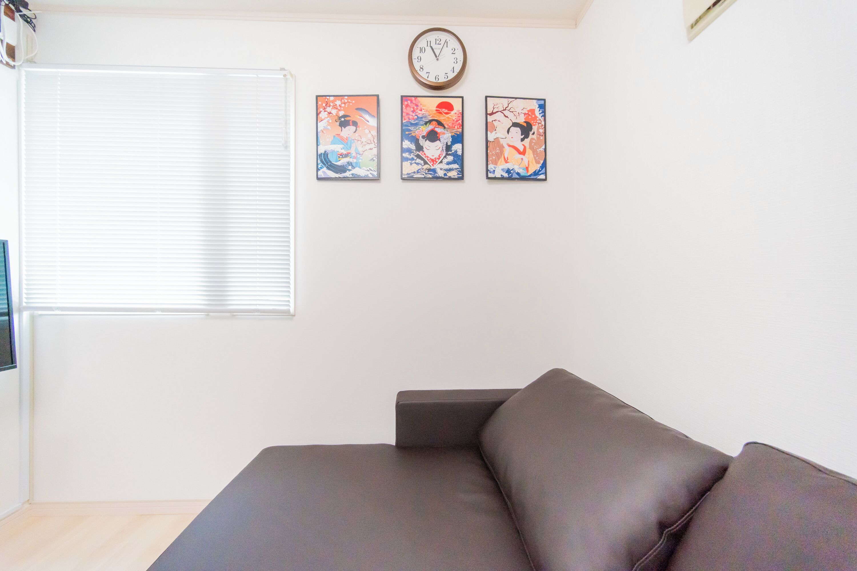 A room with a brown sofa, a wall clock, and three framed artworks.