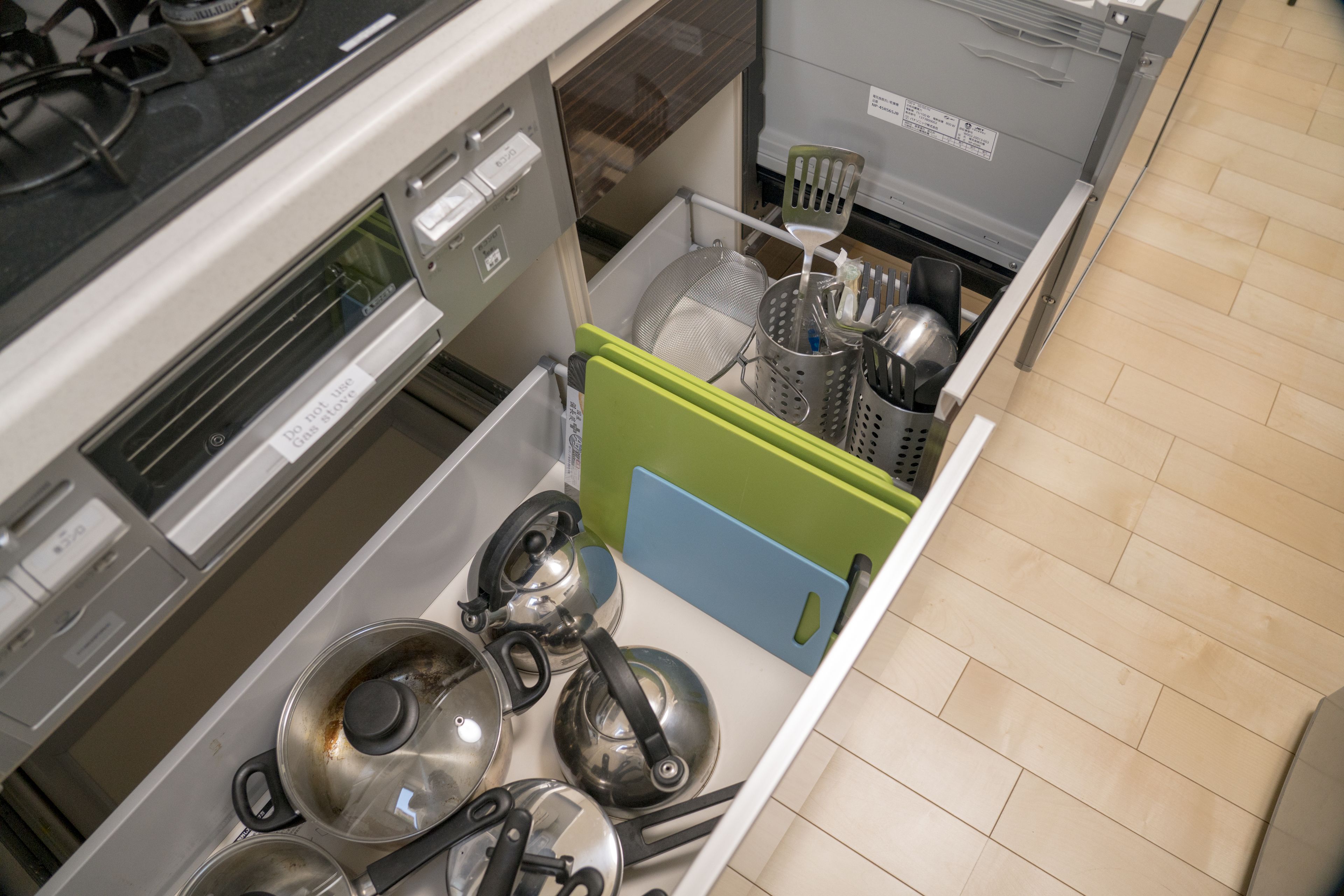 A kitchen with stainless steel appliances, including a stove and a microwave. There are pots and pans on the stove, and a green and blue storage unit is visible.