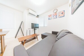 A modern living room with a grey sofa, a wooden coffee table, and a TV on a stand. There are three framed artworks on the wall and a clock. - Otsuka No Yado (Tokyo)