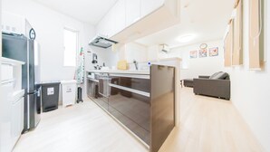 Eine moderne Küche mit Edelstahlgeräten, einem eingebauten Backofen und einem grauen Sofa im Wohnbereich.