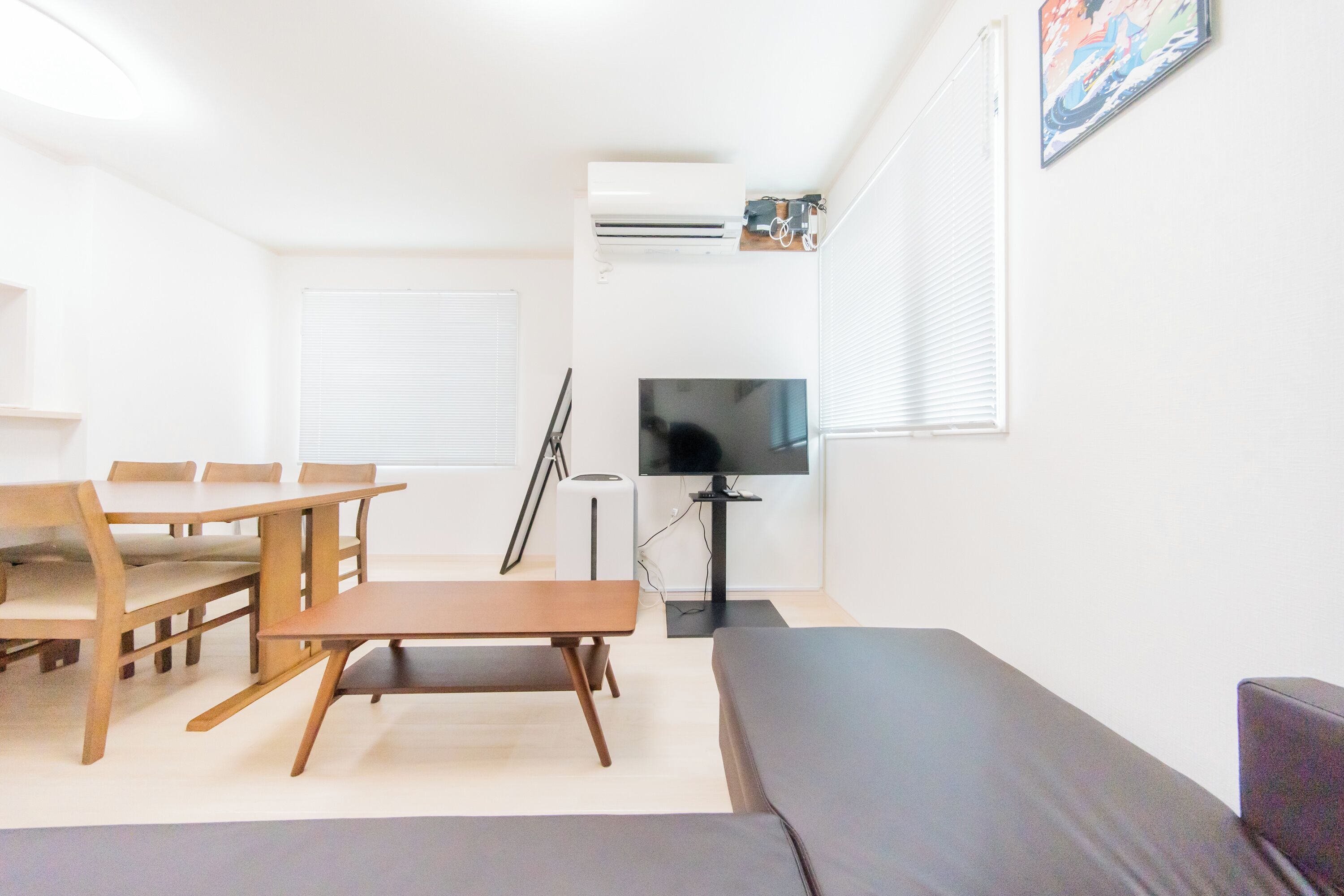 A modern living room with a sofa, a dining table with chairs, a TV, and an air conditioning unit.