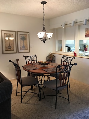 A dining area with a round table, six chairs, and a chandelier. There are two framed pictures on the wall.