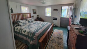 A bedroom with a wooden bed, a desk with a computer, a chair, a window, and a door. - Eagle Harbor- Harbor Pines: Savor History and Nature at Harbor Pines Cottage (Eagle Harbor)