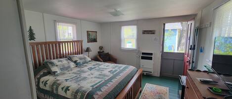 A bedroom with a wooden bed, a desk with a computer, a chair, a window, and a door.