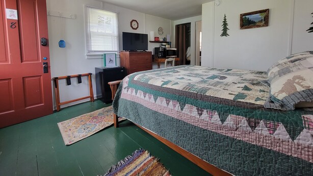A bedroom with a bed, a desk, a television, and a door. - Eagle Harbor- Harbor Pines: Savor History and Nature at Harbor Pines Cottage (Eagle Harbor)