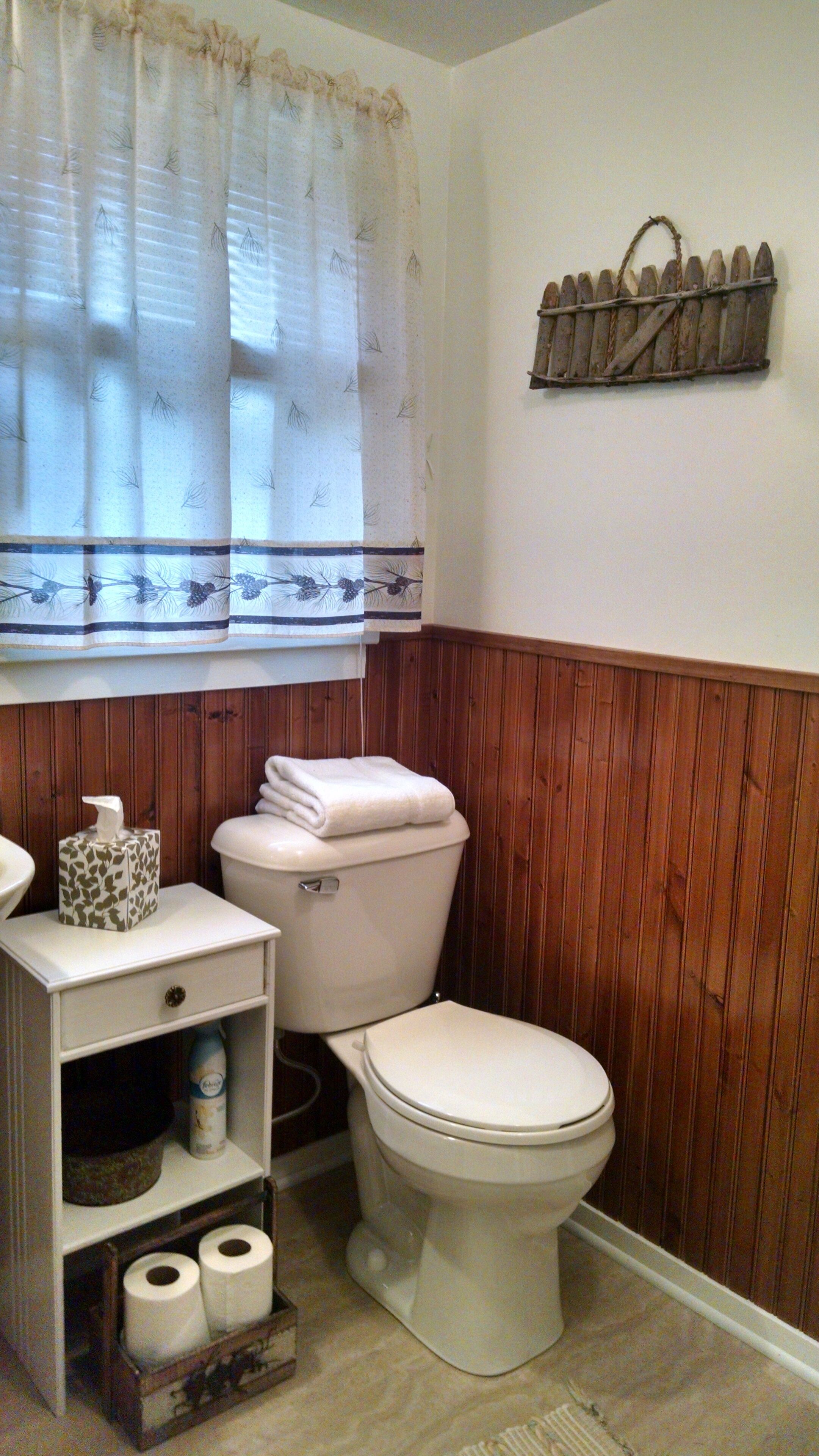 Un baño con inodoro, un estante con artículos de aseo y una ventana con cortina.