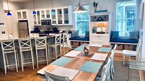 A modern kitchen with white cabinets, a dining area with a wooden table and white chairs, and a seating area with a bench and cushions. - ‘FIVESEASONS’ Beautiful PET friendly HOME 🏖 2 POOLS * SHORT WALK TO BEACH  (Santa Rosa Beach)