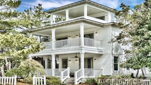 A two-story white building with a balcony, surrounded by trees and a white picket fence. - ‘FIVESEASONS’ Beautiful PET friendly HOME 🏖 2 POOLS * SHORT WALK TO BEACH  (Santa Rosa Beach)