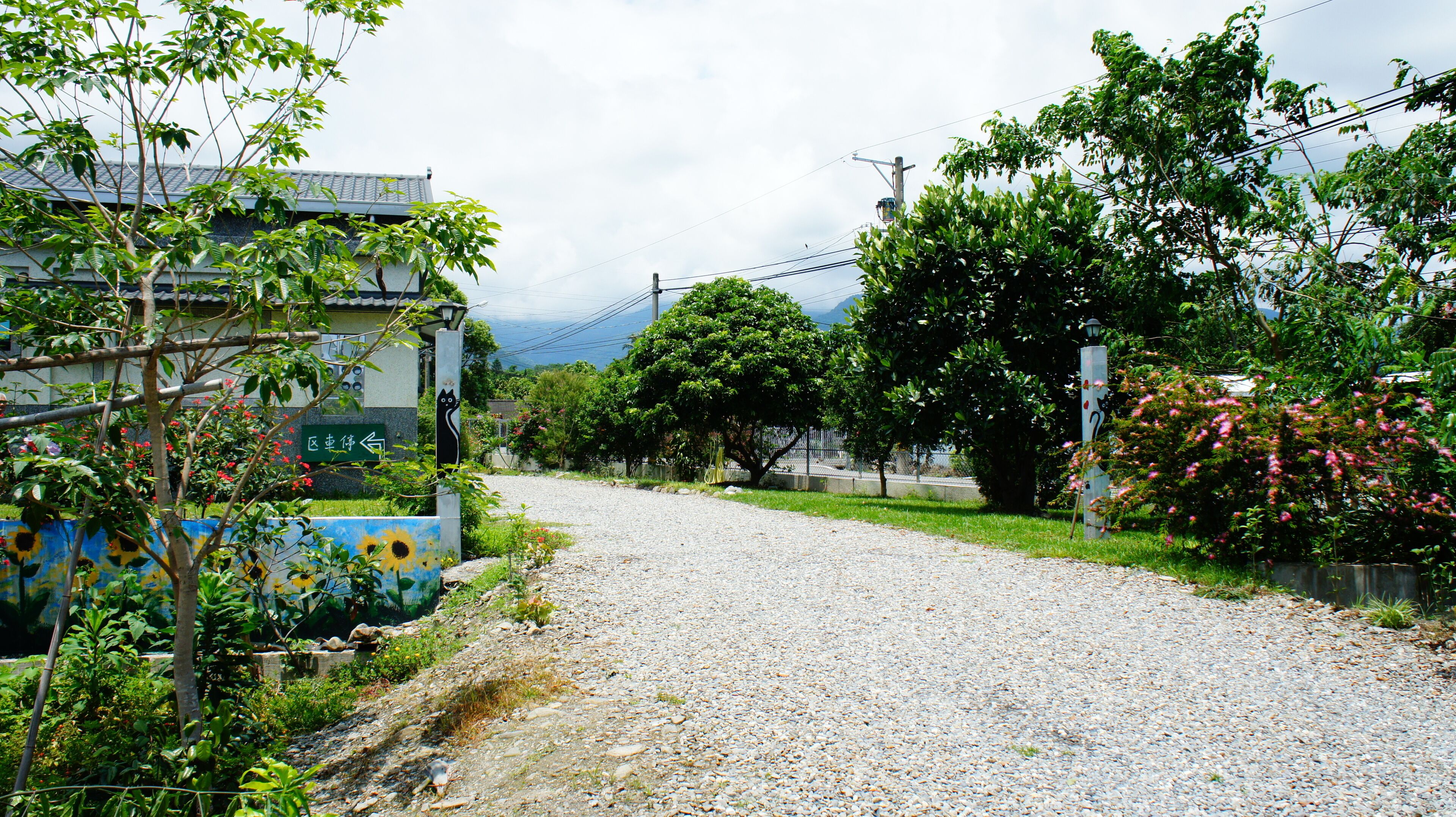 A gravel road leading to a building with a sign indicating a direction.