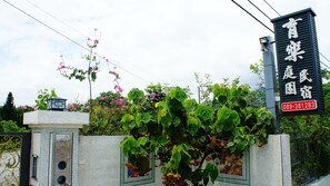 Un edificio con un letrero en idioma extranjero, una reja y abundante vegetación.