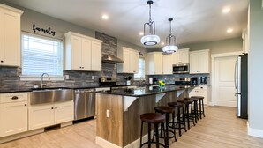 A modern kitchen with white cabinets, a stainless steel sink, a large island with bar stools, and a stone backsplash. - 10 bedrooms w/Swim/Spa - In/outdoor community pool (Branson)
