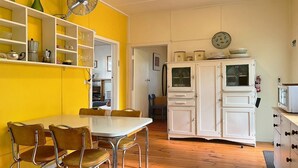 Een keuken met een eettafel, stoelen, een wit kastje en een ventilator.