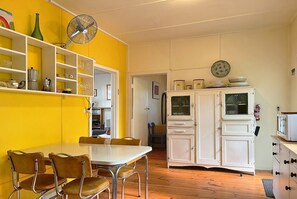 Eine Küche mit Esstisch, Stühlen, einem weißen Schrank und einem Ventilator.