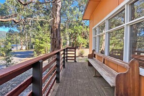 Une terrasse en bois avec une rambarde, un banc et un bâtiment doté de grandes fenêtres.