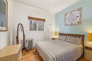 A bedroom with a bed, a window with blinds, a radiator, a wooden dresser, and a wall map.