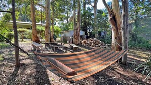 Een hangmat tussen bomen in een bebost gebied met picknicktafels en een tuinhuis.
