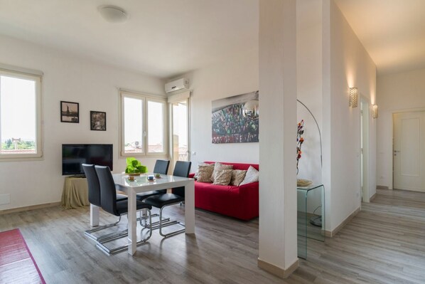 A modern living room with a dining table, red sofa, and a TV.